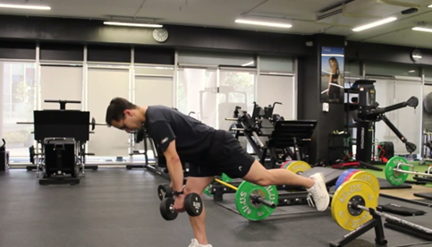 Hombre realizando peso muerto unilateral con mancuernas en el gimnasio.